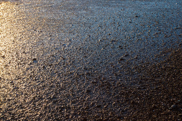 Sand and stones on the seashore after a surging wave in the sunset rays of the sun. background image. Tourism in Abkhazia.