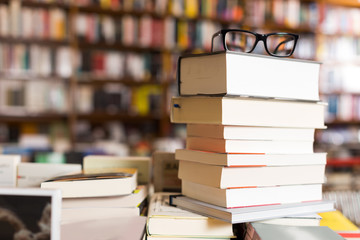 glasses on top of stack of books lying on table in bookstore