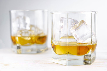 Two glasses of scotch whiskey with ice cubes, white background, wooden backdrop