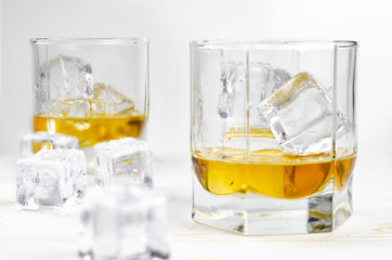 Two glasses of scotch whiskey with ice cubes, white background, wooden backdrop