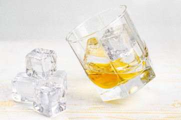 Glasses of scotch whiskey with ice cubes, white background, wooden backdrop