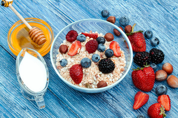 Greek yogurt granola and berry mix. Top view. Delicious healthy muesli with raspberry, blueberry, strawberry, hazelnut, BlackBerry, milk and honey on blue wooden rustic table