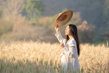 Selective focus medium shot of young beautiful asian women taking off vietnamese hat standing and smiling in golden and green wheat field in the morning sunny day.