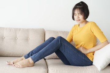 Fototapeta premium Young asian woman sit on sofa in the living room. she having painful stomachache.