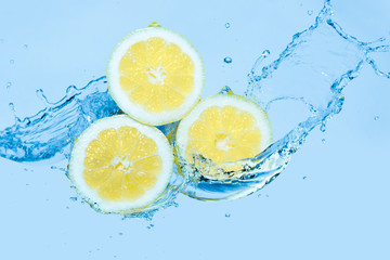 Fototapeta na wymiar Water splashing on slices of lemon against a light blue background
