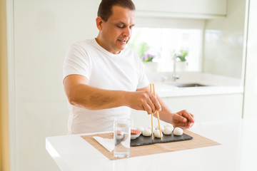 Middle age man eating asian dim sum using chopsticks at home