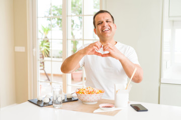 Middle age man eating asian food with chopsticks at home smiling in love showing heart symbol and shape with hands. Romantic concept.