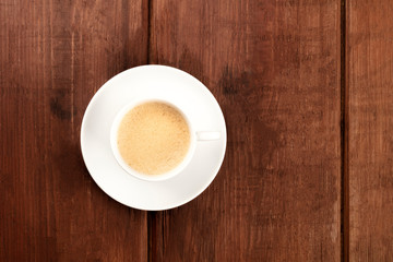 A photo of coffee in a simple white cup, shot from the top on a dark rustic wooden background with a place for text