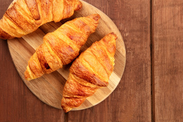 An overhead photo of three croissants on a dark rustic wooden background with a place for text