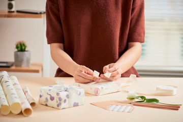 Detail of woman hands packing some presents with gift paper