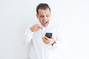 Middle age man using smartphone over white wall very happy pointing with hand and finger