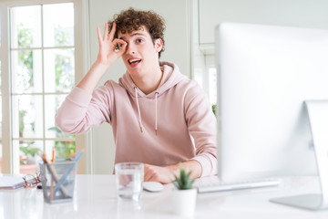 Young student man using computer with happy face smiling doing ok sign with hand on eye looking through fingers