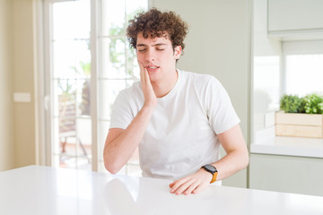 Young handsome man wearing white t-shirt at home touching mouth with hand with painful expression because of toothache or dental illness on teeth. Dentist concept.