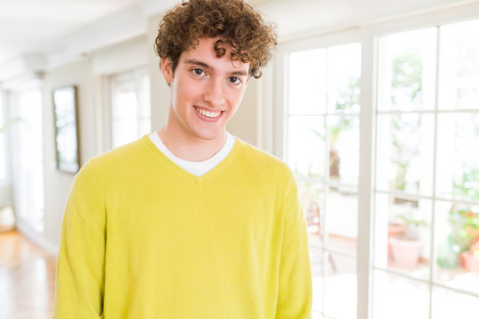 Young handsome man wearing yellow sweater at home with a happy and cool smile on face. Lucky person.