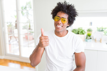 African American man wearing glasses doing happy thumbs up gesture with hand. Approving expression looking at the camera showing success.