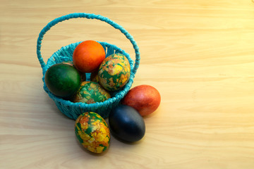 Easter eggs lying on a yellow wooden table and in a blue basket, copy pastes