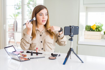 Beautiful young influencer woman recording make up video tutorial with surprise face pointing finger to himself