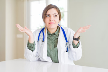 Beautiful young doctor woman wearing medical coat and stethoscope clueless and confused expression...