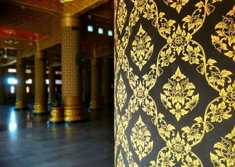 Close up golden traditional patterns of wooden column and blurred inside of downstairs area background of the large Thai temple