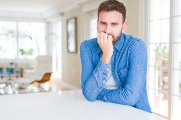 Handsome man at home looking stressed and nervous with hands on mouth biting nails. Anxiety problem.