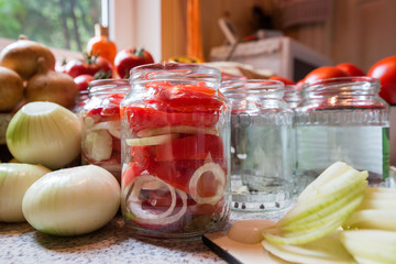 Canning fresh tomatoes with onions in jelly marinade. Woman hands putting red ripe tomato slices and onion rings in jars. Basil, parsley leaves on top of onions. Vegetable salads for winter