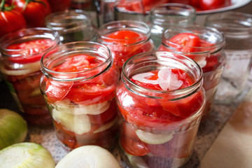Canning fresh tomatoes with onions in jelly marinade. Woman hands putting red ripe tomato slices and onion rings in jars. Basil, parsley leaves on top of onions. Vegetable salads for winter