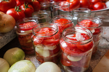 Canning fresh tomatoes with onions in jelly marinade. Woman hands putting red ripe tomato slices and onion rings in jars. Basil, parsley leaves on top of onions. Vegetable salads for winter