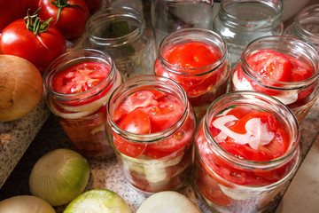 Canning fresh tomatoes with onions in jelly marinade. Woman hands putting red ripe tomato slices and onion rings in jars. Basil, parsley leaves on top of onions. Vegetable salads for winter