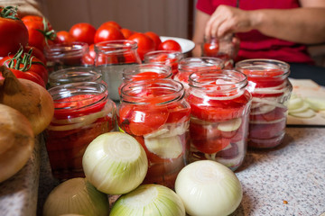 Canning fresh tomatoes with onions in jelly marinade. Woman hands putting red ripe tomato slices and onion rings in jars. Basil, parsley leaves on top of onions. Vegetable salads for winter