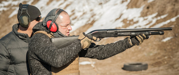 Instructor on shooting range teaches student to shoot with shotgun