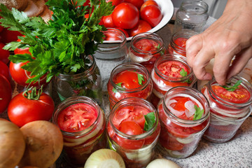 Canning fresh tomatoes with onions in jelly marinade. Woman hands putting red ripe tomato slices and onion rings in jars. Basil, parsley leaves on top of onions. Vegetable salads for winter