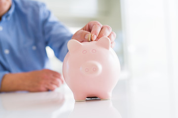 Obraz na płótnie Canvas Close up of man putting a coin inside of piggy bank as savings