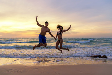 Fototapeta na wymiar Summer Vacation. Couple jumping holding hands on tropical on the beach sunset time in holiday trips. Honeymoon holidays people relaxing together on summer travel destination. Summer Travel 