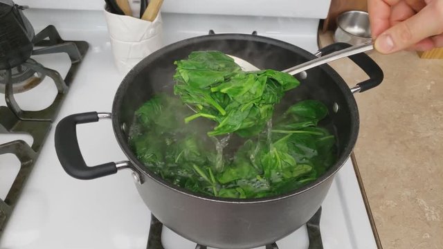 Home cooking - Pushing down and checking baby spinach being blanched in non stick pot of hot water with lid off.