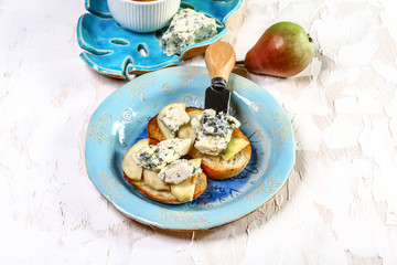 Toasted bread with tasty cheese and pear on wooden board. on a blue ceramic plate