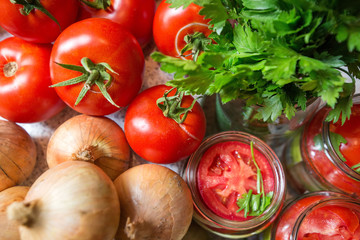 Canning fresh tomatoes with onions in jelly marinade. Woman hands putting red ripe tomato slices and onion rings in jars. Basil, parsley leaves on top of onions. Vegetable salads for winter