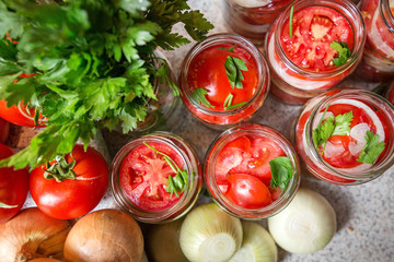 Canning fresh tomatoes with onions in jelly marinade. Woman hands putting red ripe tomato slices and onion rings in jars. Basil, parsley leaves on top of onions. Vegetable salads for winter