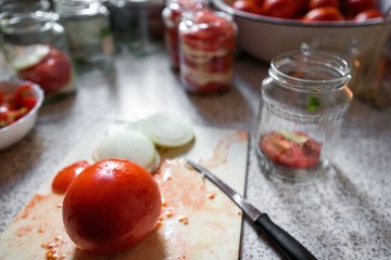 Canning fresh tomatoes with onions in jelly marinade. Woman hands putting red ripe tomato slices and onion rings in jars. Basil, parsley leaves on top of onions. Vegetable salads for winter
