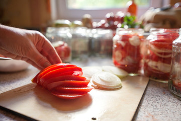 Canning fresh tomatoes with onions in jelly marinade. Woman hands putting red ripe tomato slices and onion rings in jars. Basil, parsley leaves on top of onions. Vegetable salads for winter