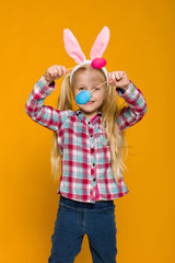 Portrait of cute little child girl with Easter bunny ears holding colorful eggs on yellow background. Happy easter