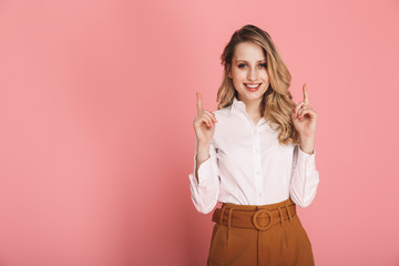 Portrait of beautiful woman smiling and pointing fingers at copyspace isolated over pink background