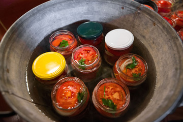 Canning fresh tomatoes with onions in jelly marinade. Conservation and cooking. Jars boiling in water to kill bacteria. Sealing process.  Basil, parsley leaves on top. Vegetable salads for winter