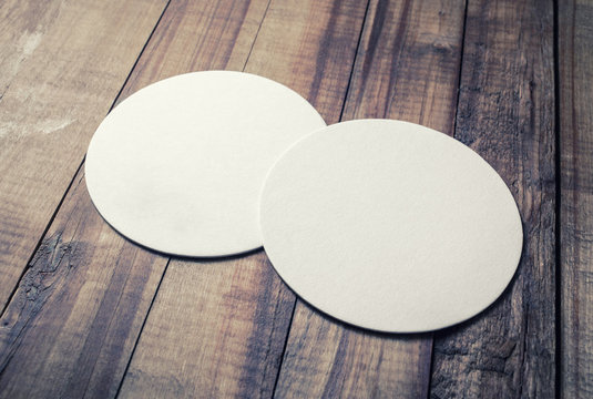 Photo of two blank beer coasters on wooden background.