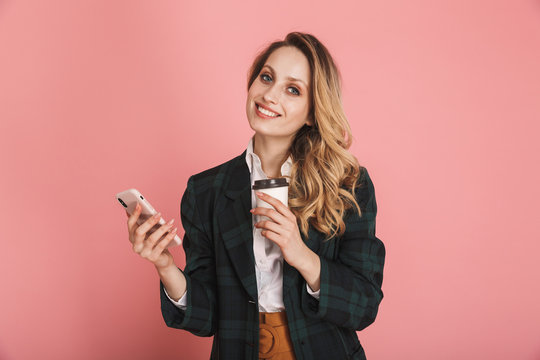 Image of pretty woman using mobile phone and drinking takeaway coffee isolated over pink background