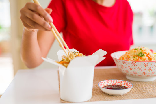 Close up of young woman eating noodles from delivery box using choopsticks