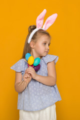 Obraz na płótnie Canvas Portrait of cute little child girl with Easter bunny ears holding colorful eggs on yellow background. Happy easter