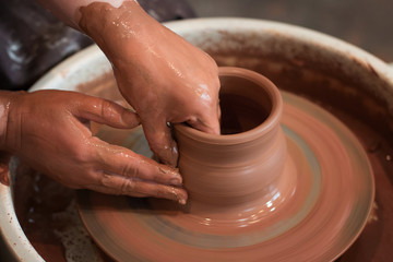 Rotating potter's wheel and clay ware on it taken from above. A sculpts his hands with a clay cup on a potter's wheel. Hands in clay. 