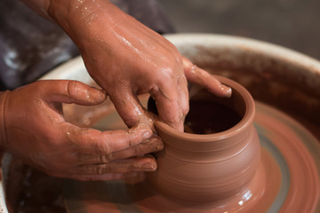 Rotating potter's wheel and clay ware on it taken from above. A sculpts his hands with a clay cup on a potter's wheel. Hands in clay. 
