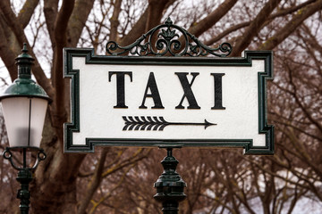 Old vintage retro style taxi station sign with arrow to the right, lantern lamp post and trees in...