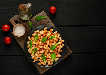 Delicious Italian pasta with tomato sauce, on a plate on a dark wooden table. View from above